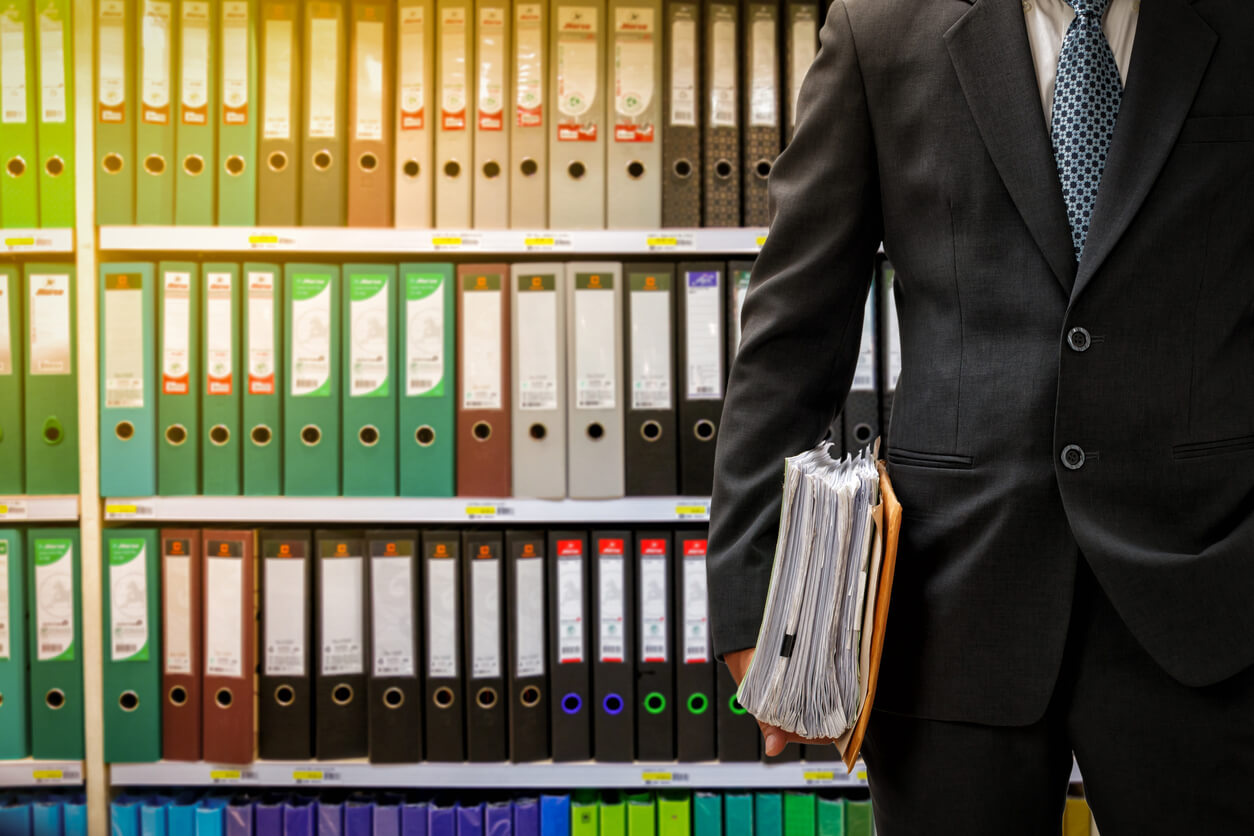 A man in suit and tie standing next to shelves of binders.